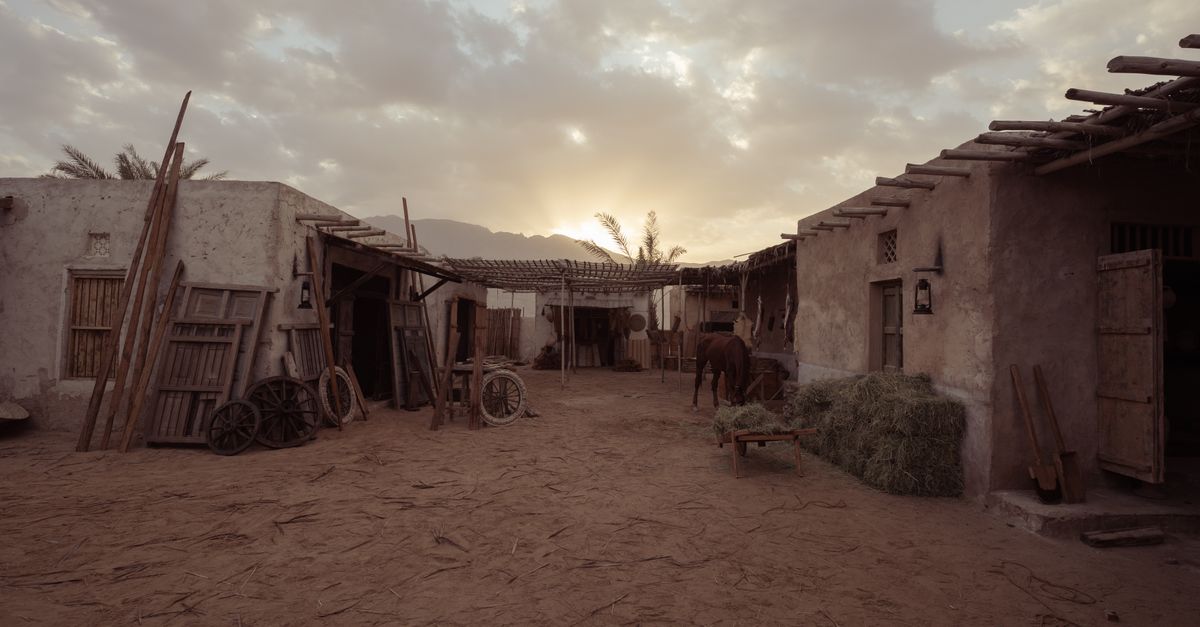 Rustic desert village scene with adobe houses and a horse at sunset.