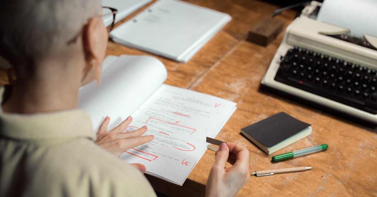 An adult woman reviewing a script with red pen marks at a wooden desk with a typewriter.