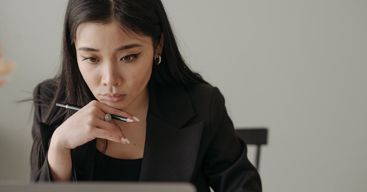 Young woman working remotely, focused on laptop in home office, holding a pencil.